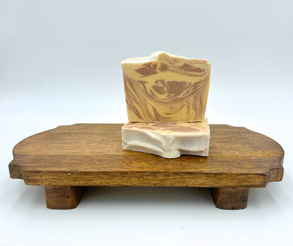Two pieces of marbled soap on a wooden stand against a white background