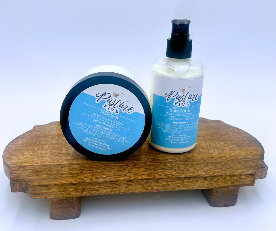 Two containers of goat milk lotion from Pasture Five on a wooden stand with a white background