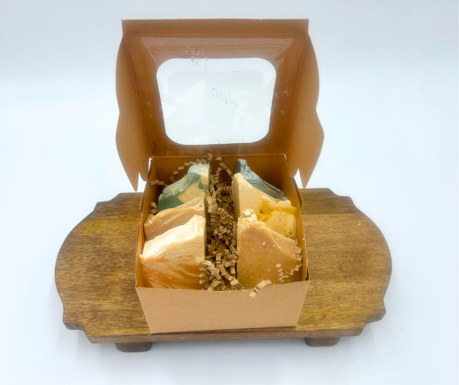 Wooden display stand with a box containing various types of goat milk soap on a white background