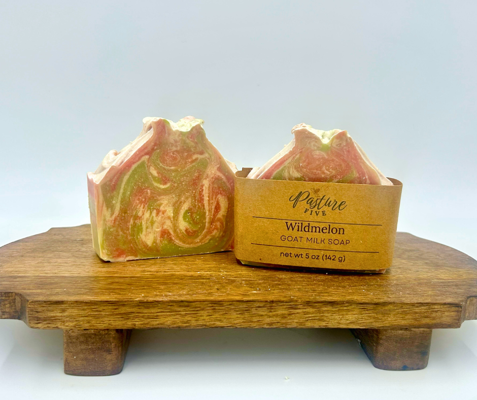 Two wildmelon goat milk soaps with a wooden box on a white background