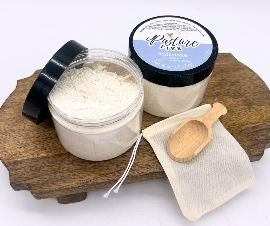two containers of Bath Soaks, spoon on a wooden board. 