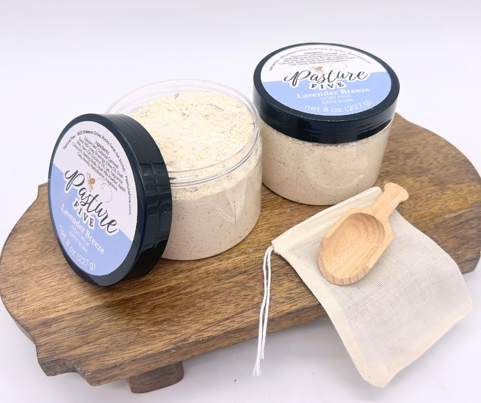 two containers of Bath Soaks, spoon on a wooden board. 