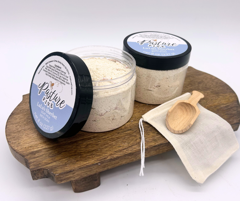 two containers of Bath Soaks, spoon on a wooden board. 