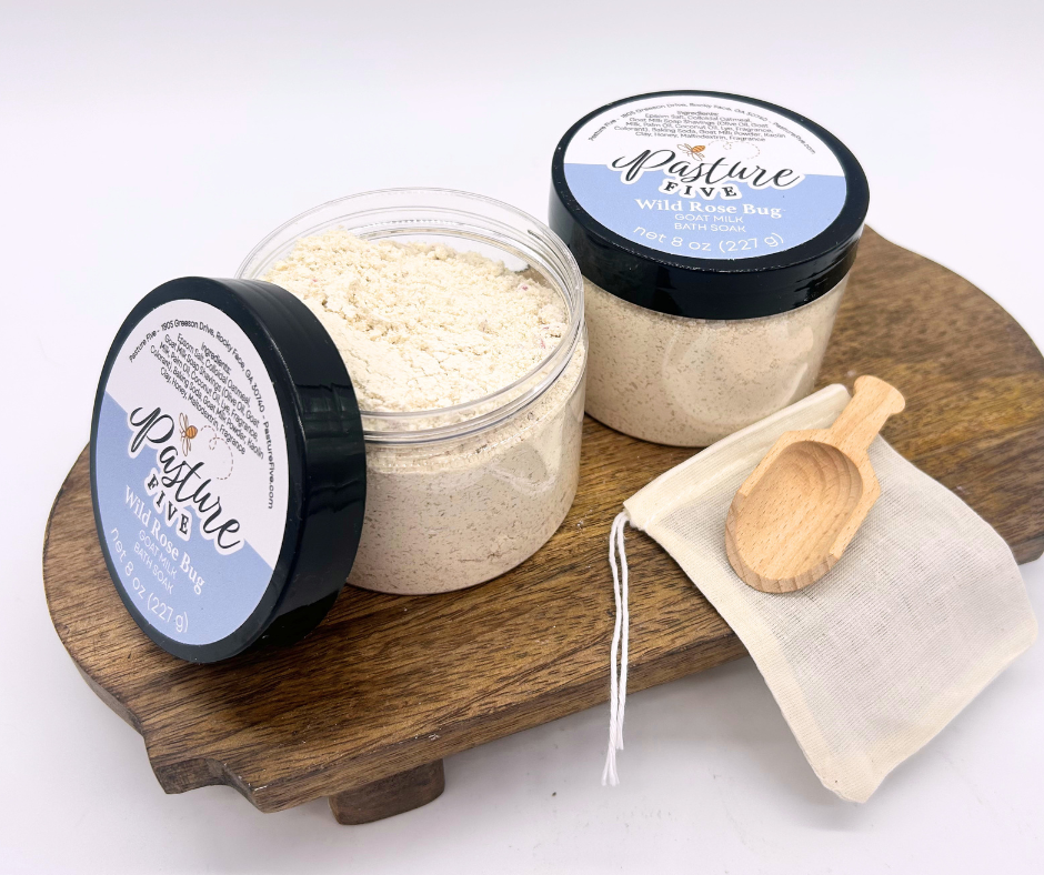 two containers of Bath Soaks, spoon on a wooden board. 