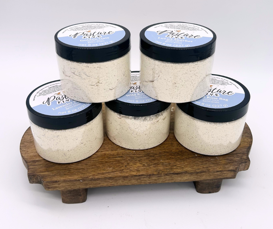 Set of six jars of bath soaks  on a wooden stand against a white background