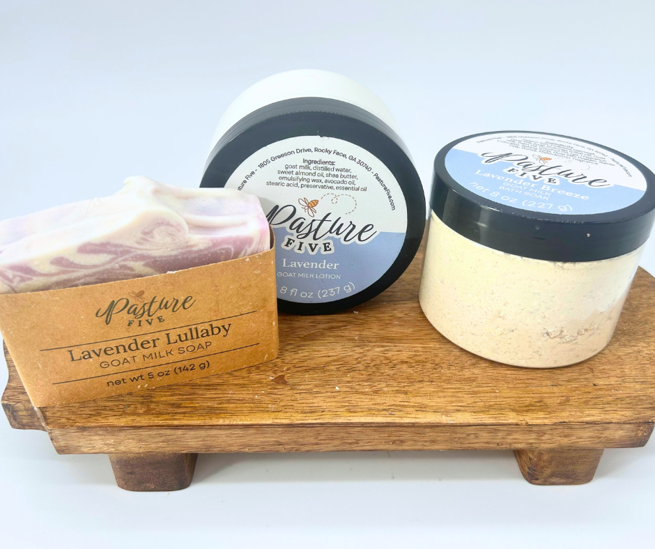 A jar of lotion, soap bar, and jar of bath soaks on a wood board.