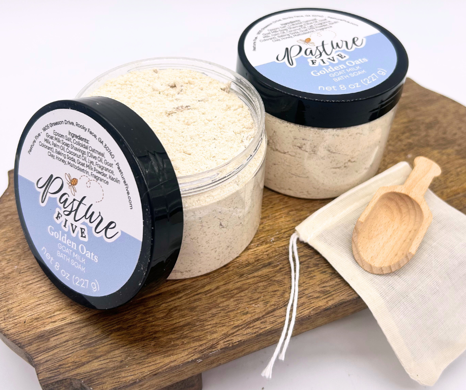 two containers of Bath Soaks, spoon on a wooden board. 