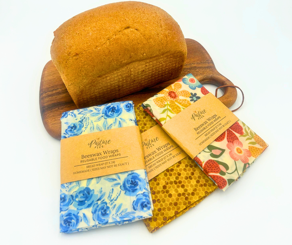 Beeswax wraps with floral designs  and a loaf of bread on a white background