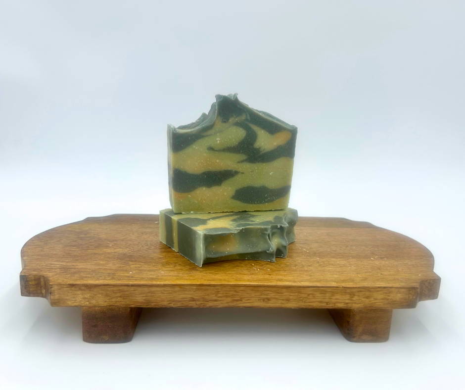 Green and brown goat milk soap on a wooden stand against a white background