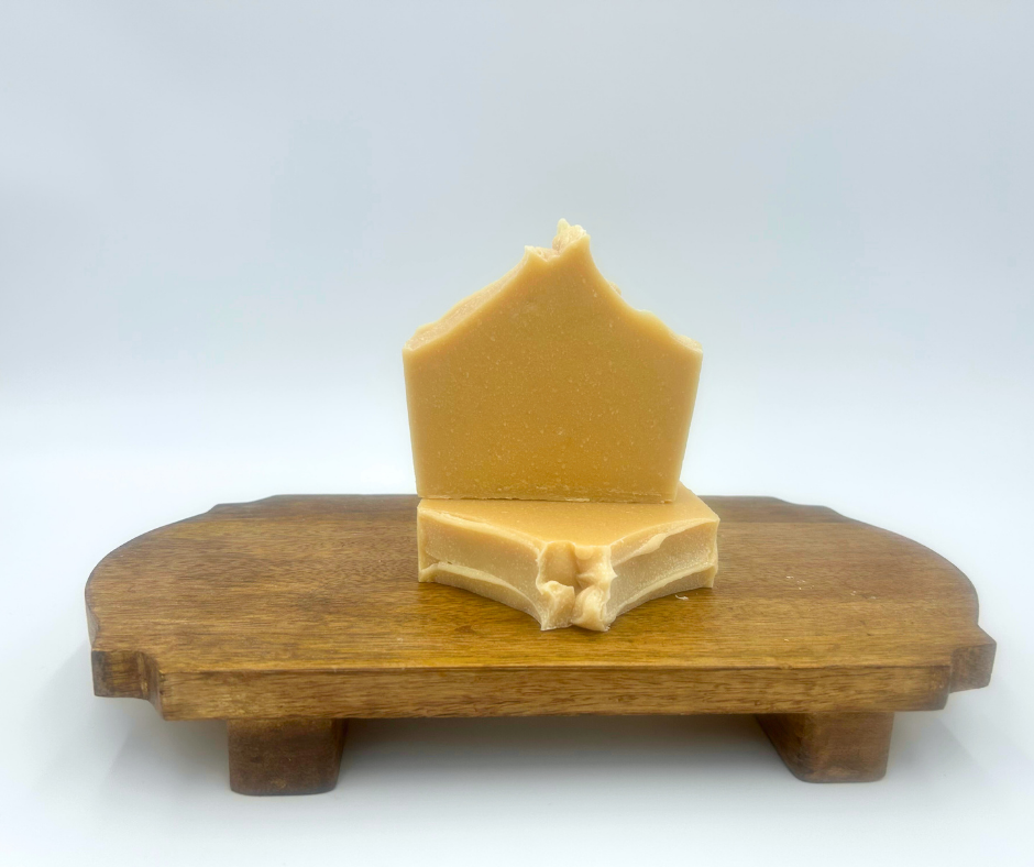 Bar of yellow goat milk soap on a wooden stand against a white background