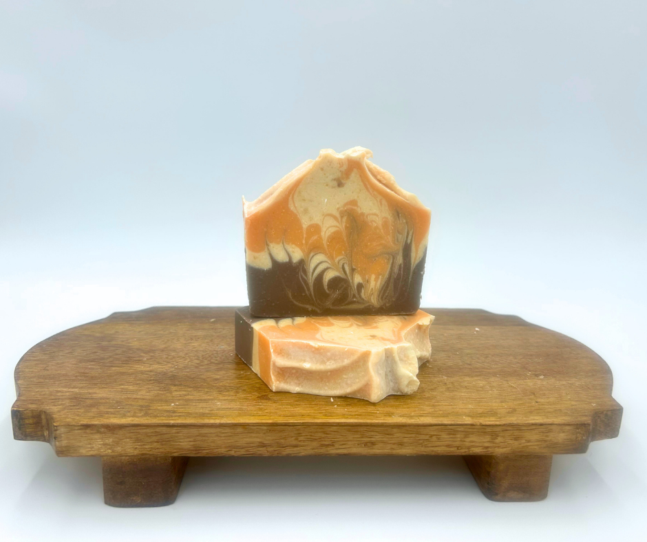 Two pieces of swirl goat milk soap on a wooden stand with a white background