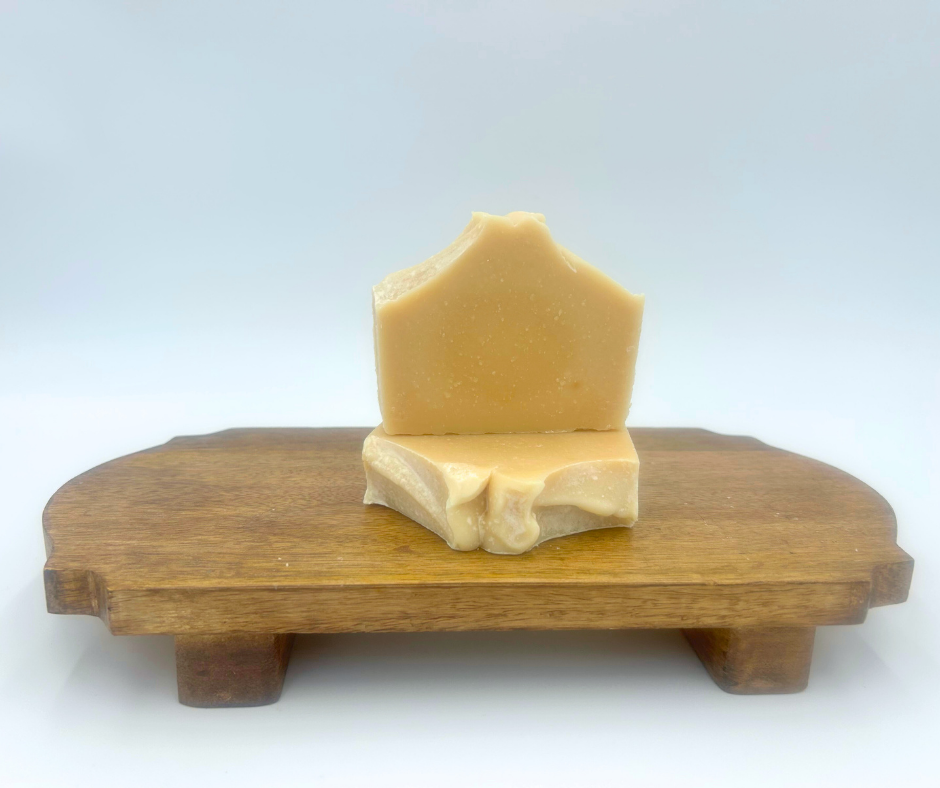 Two pieces of goat milk soap on a wooden stand against a white background