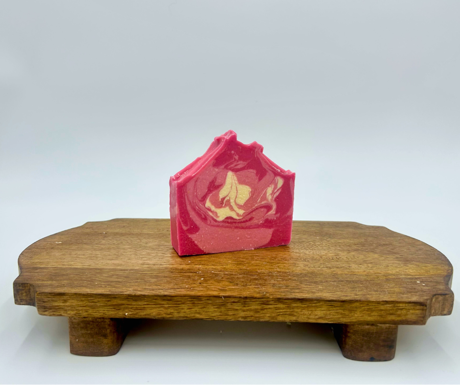 Pink and white soap bar with a design on a wooden stand against a white background