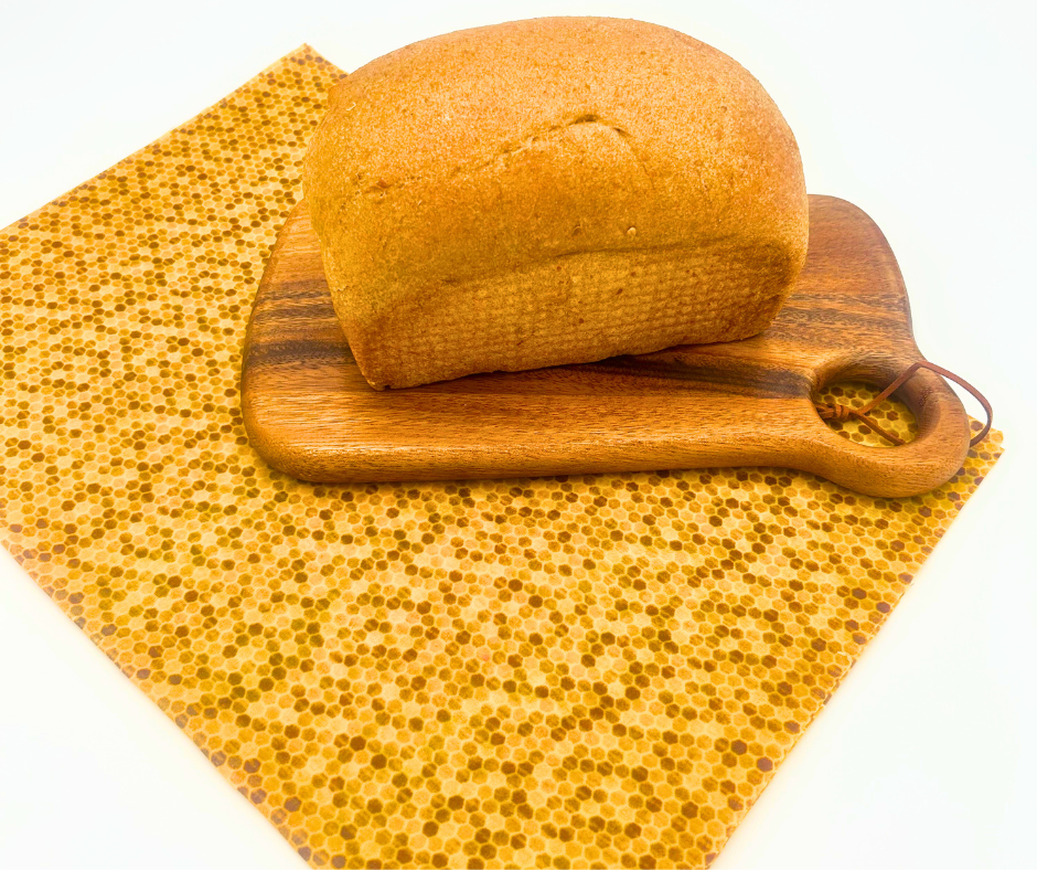 Loaf of bread on a wooden cutting board with a honeycomb patterned bread wrap underneath