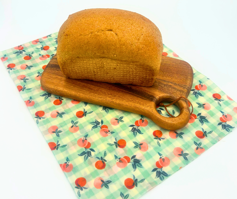 Loaf of bread on a wooden cutting board with a floral-patterned bread wrap underneath