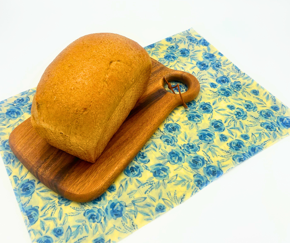 Loaf of bread on a wooden cutting board with a floral-patterned yellow bread wrap underneath