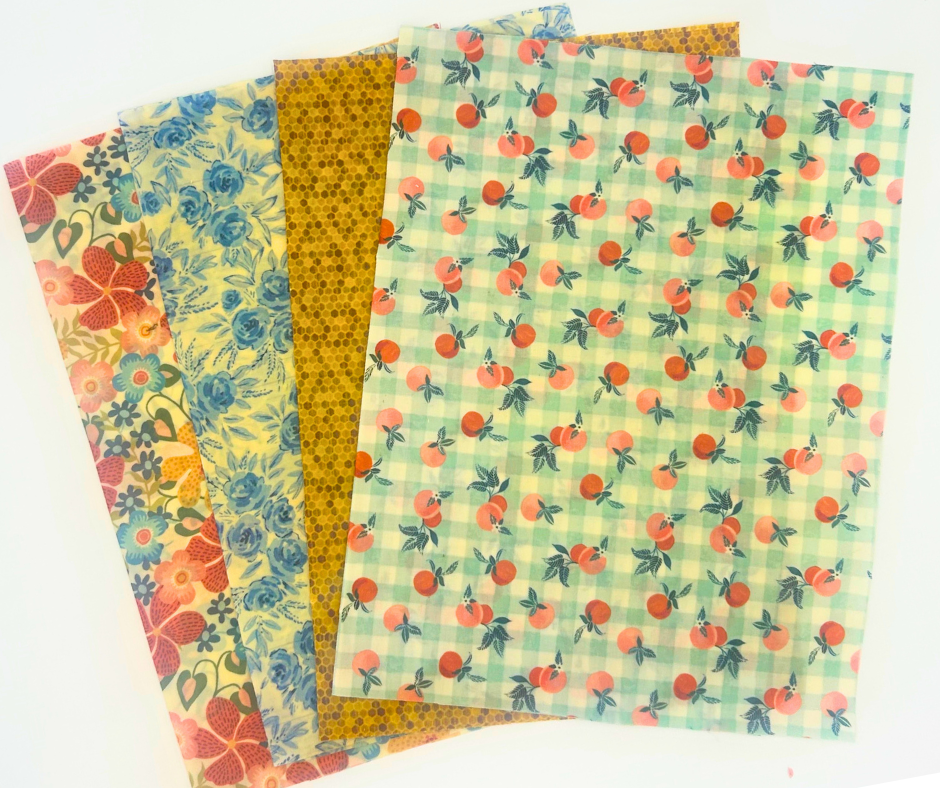 Four sheets of patterned wax wraps with floral, honey comb, and fruit designs on a white background.