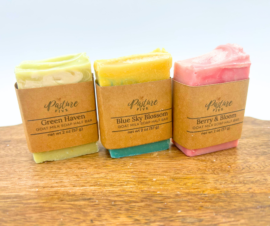 Three bars of soap in brown paper packaging on a wooden surface with a light blue background.