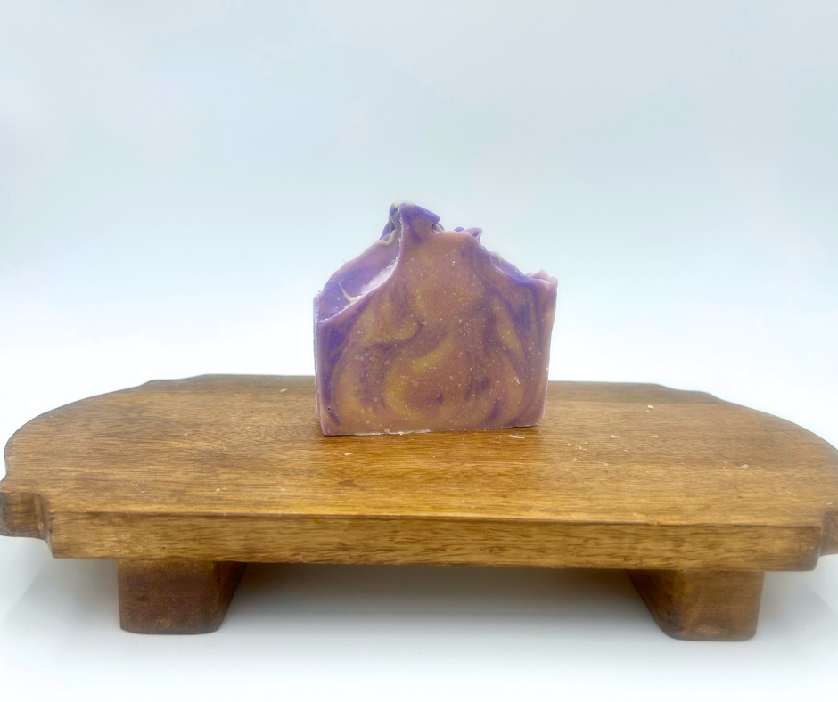Purple swirl goat milk soap on a wooden stand with a white background