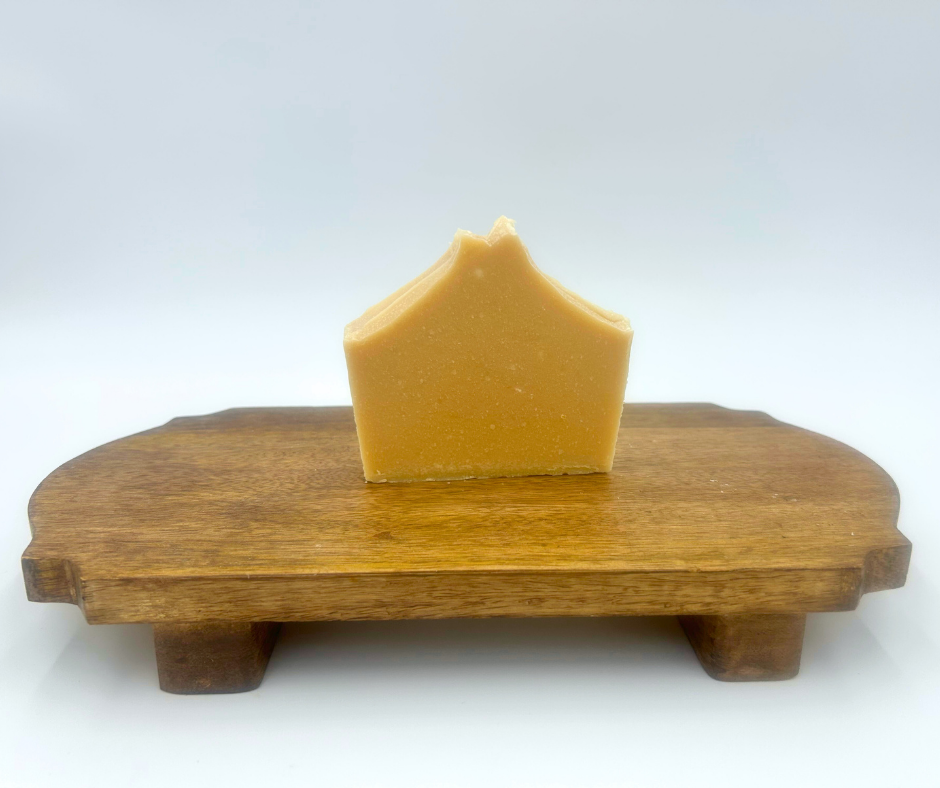Bar of goat milk soap on a wooden stand against a white background