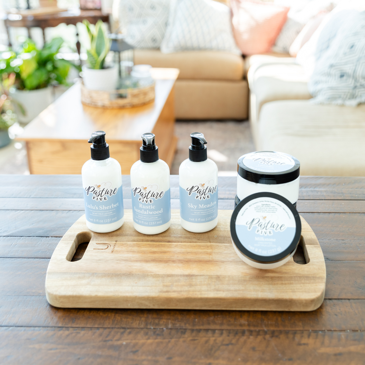 Set of goat milk lotions on a wooden tray with a blurred indoor background