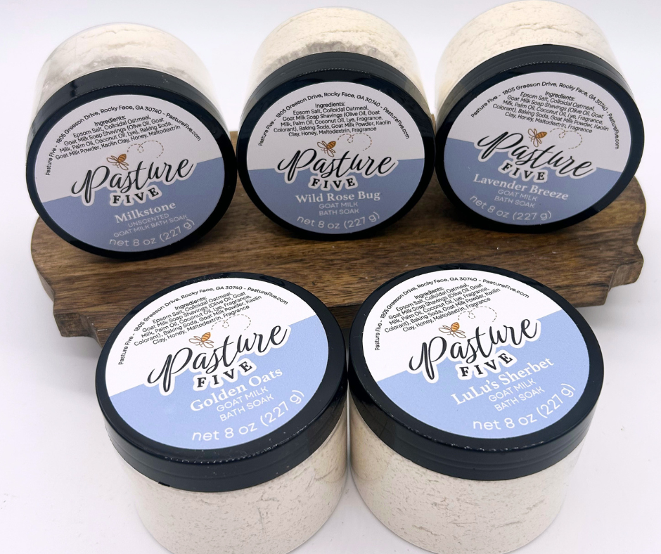 Five jars of 'Pasture Five' bath soaks on a wooden stand with visible labels.