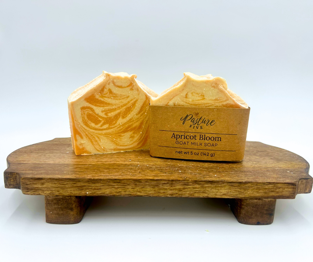 Two bars of apricot bloom goat milk soap on a wooden stand with a white background