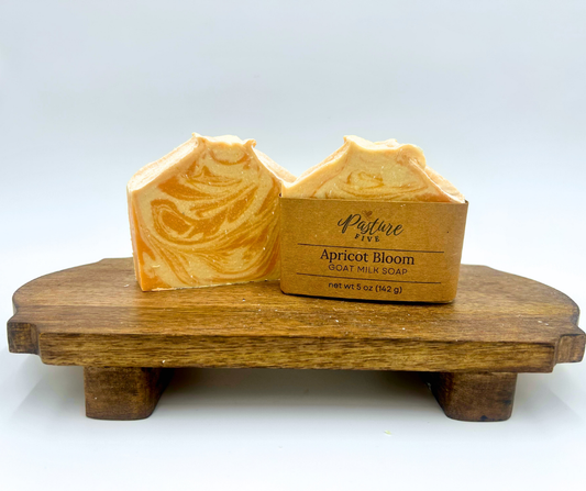 Two bars of apricot bloom goat milk soap on a wooden stand with a white background
