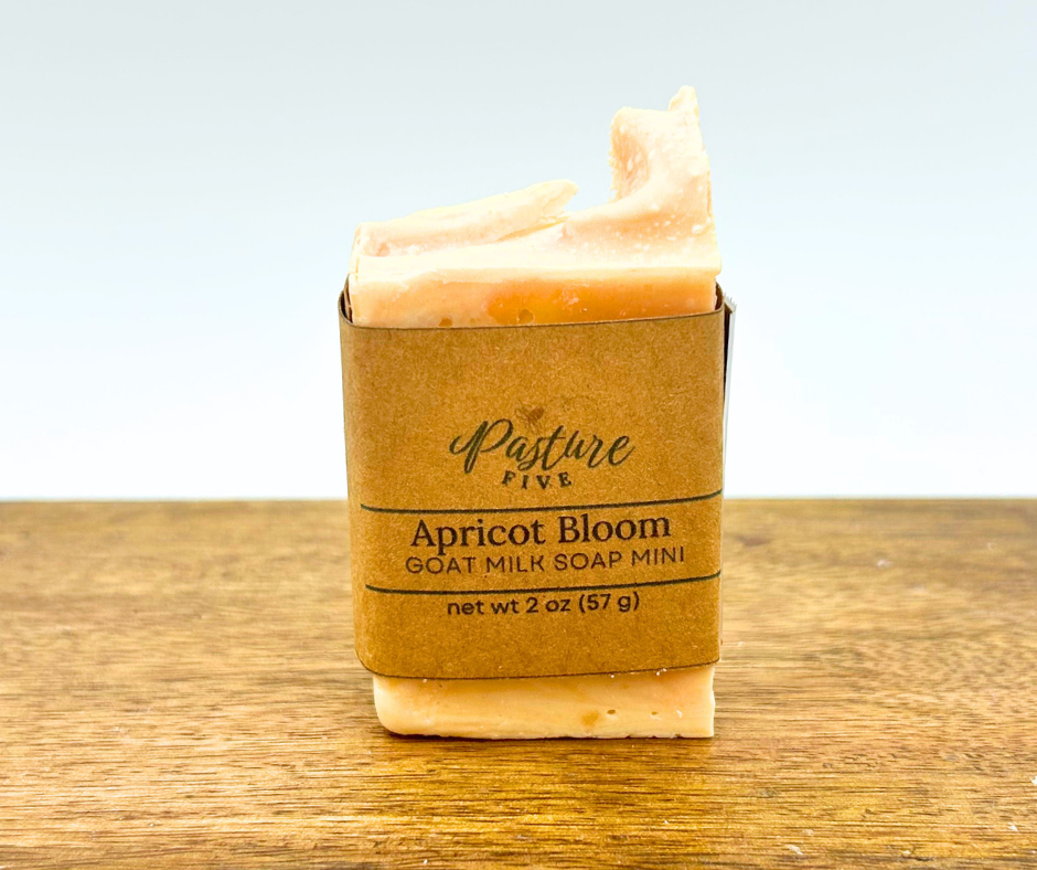 Small goat milk soap bar in a brown paper packaging with 'Pasture Five' branding on a wooden surface.