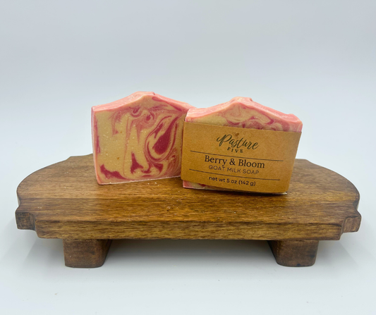 two white and pink swirl goat milk soaps on a brown stand 