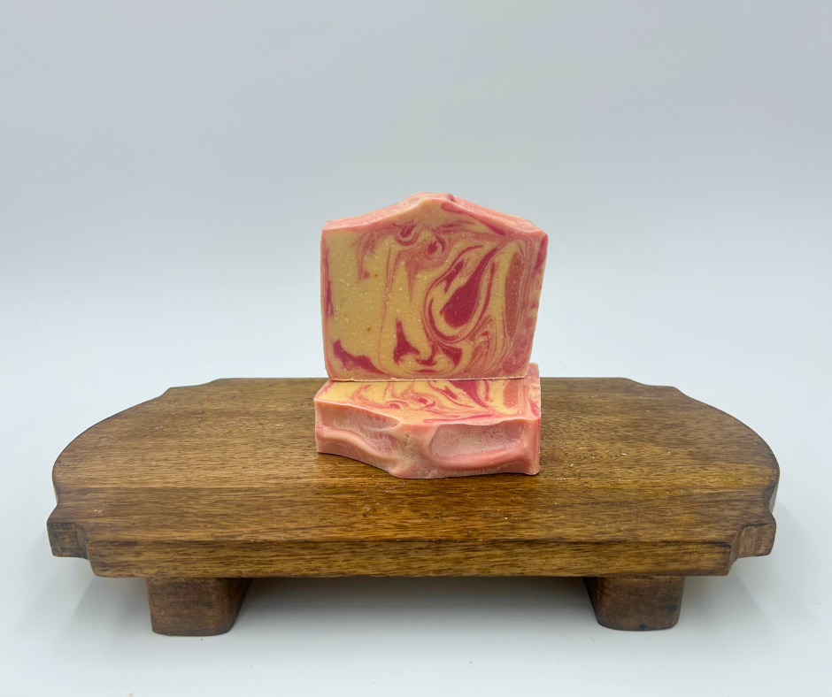 two white and pink swirl goat milk soaps on a brown stand 
