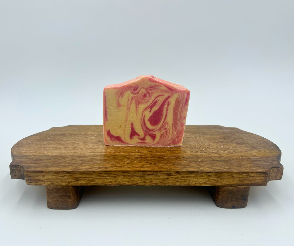 a white and pink swirl goat milk soap on a brown stand 