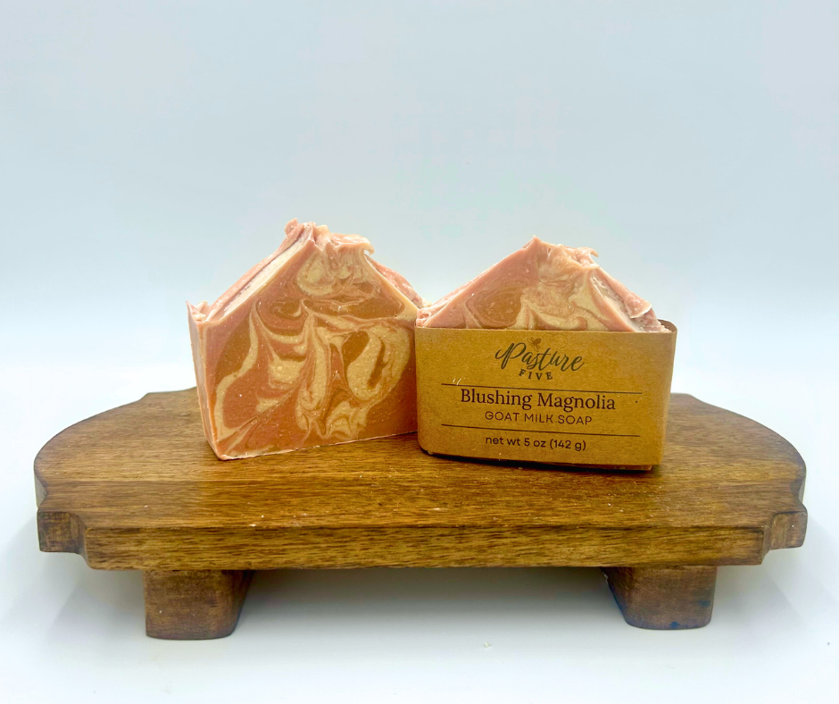 Two bars of goat milk soap with a wooden stand on a white background