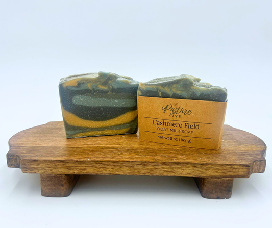 Two bars of soap on a wooden stand with a label reading 'Cashmere Field' on a white background.