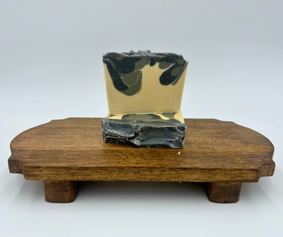 Two bars of soap with black and gray pattern on a wooden stand against a white background