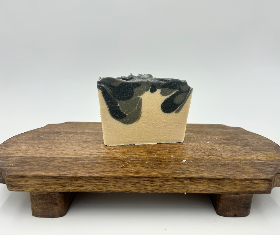 Bar of soap with black, gray and white layers on a wooden stand against a white background