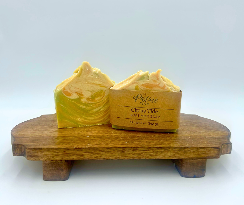 Two bars of yellow goat milk soap on a wooden stand with a white background