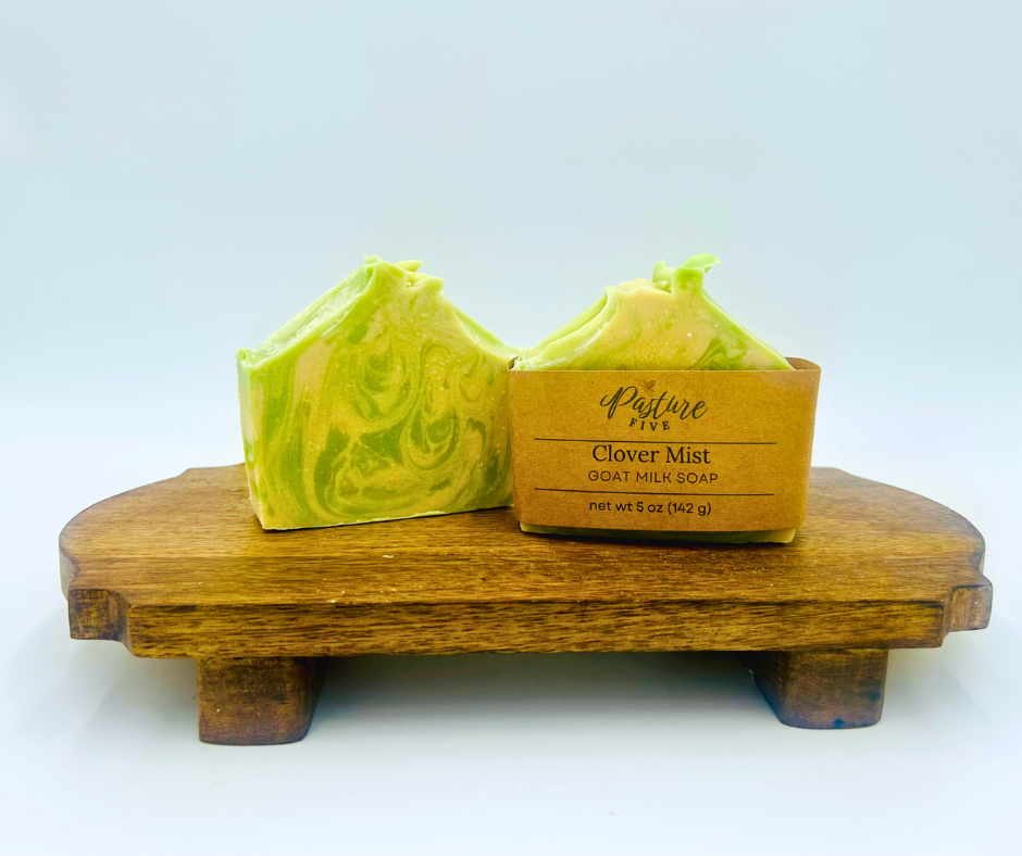 Two green-swirled goat milk soap bars on a wooden stand with a white background