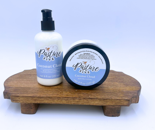 Two bottles of 'Pasture Five' Coconut Cloud lotions on a wooden stand with a light blue background.