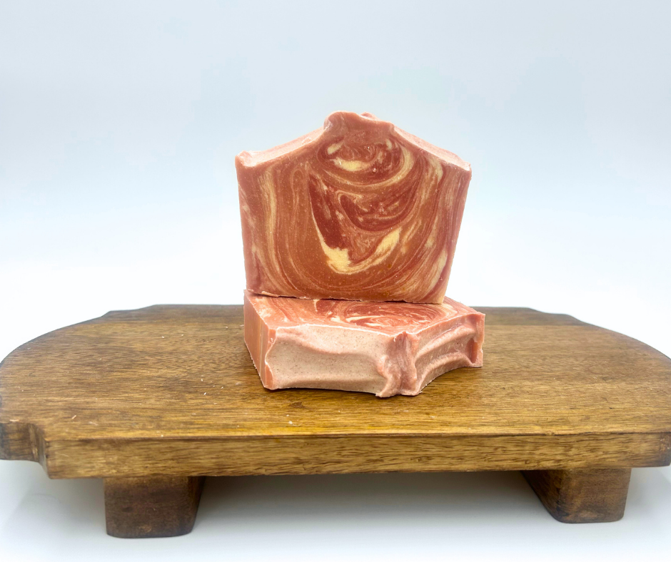 Two Cranberry Pine Goat Milk Soaps with a swirl design stacked on a wooden stand with a white background.