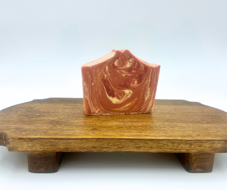 A Cranberry Pine Goat Milk Soap with a swirl design on a wooden stand with a white background.