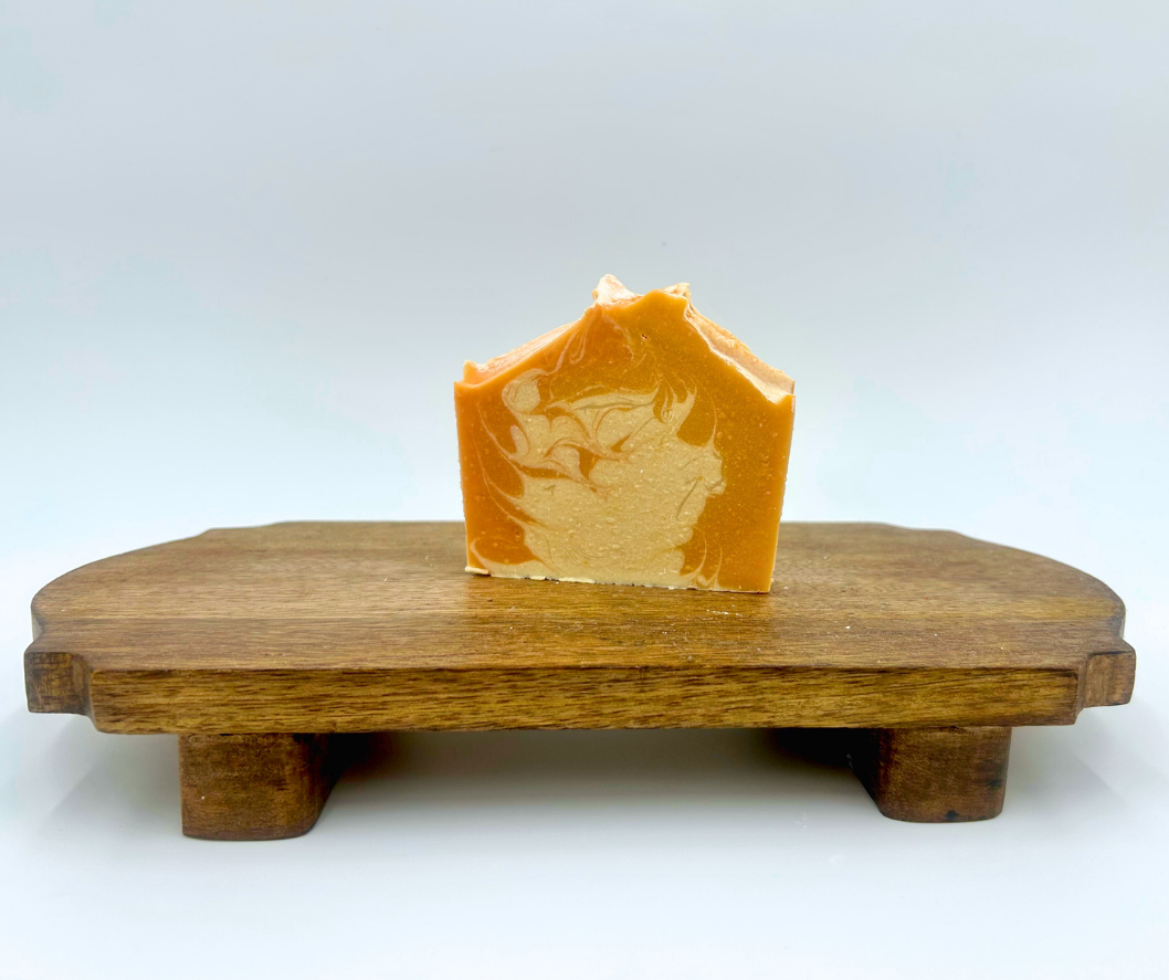 Bar of orange soap on a wooden stand with a white background
