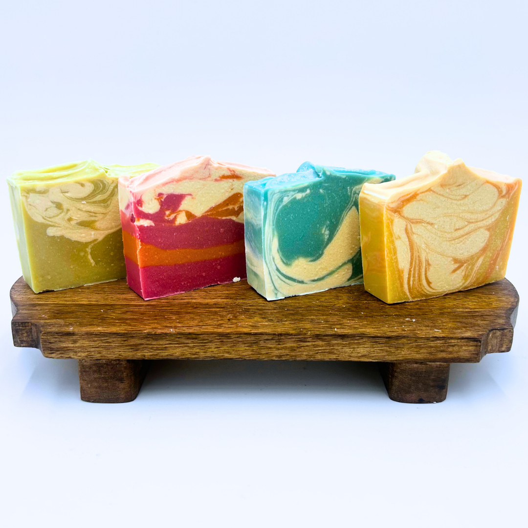 Four colorful soap bars on a wooden stand with a white background. The Summer Collection.