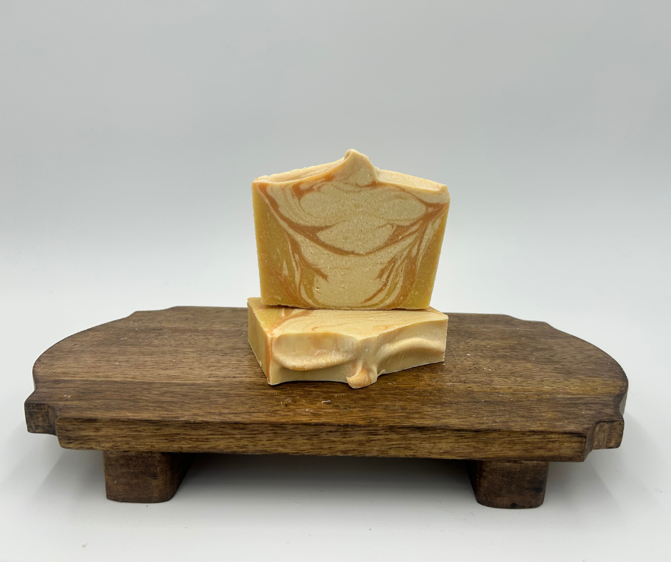 two yellow, orange and white swirl goat milk soaps on a brown stand 