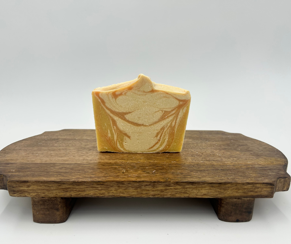 one yellow, orange and white swirl goat milk soap on a brown stand 