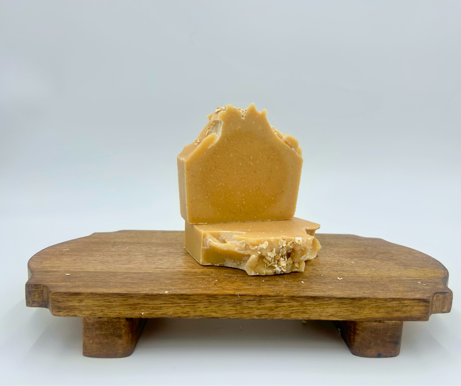 Bar of goat milk soap on a wooden stand against a white background