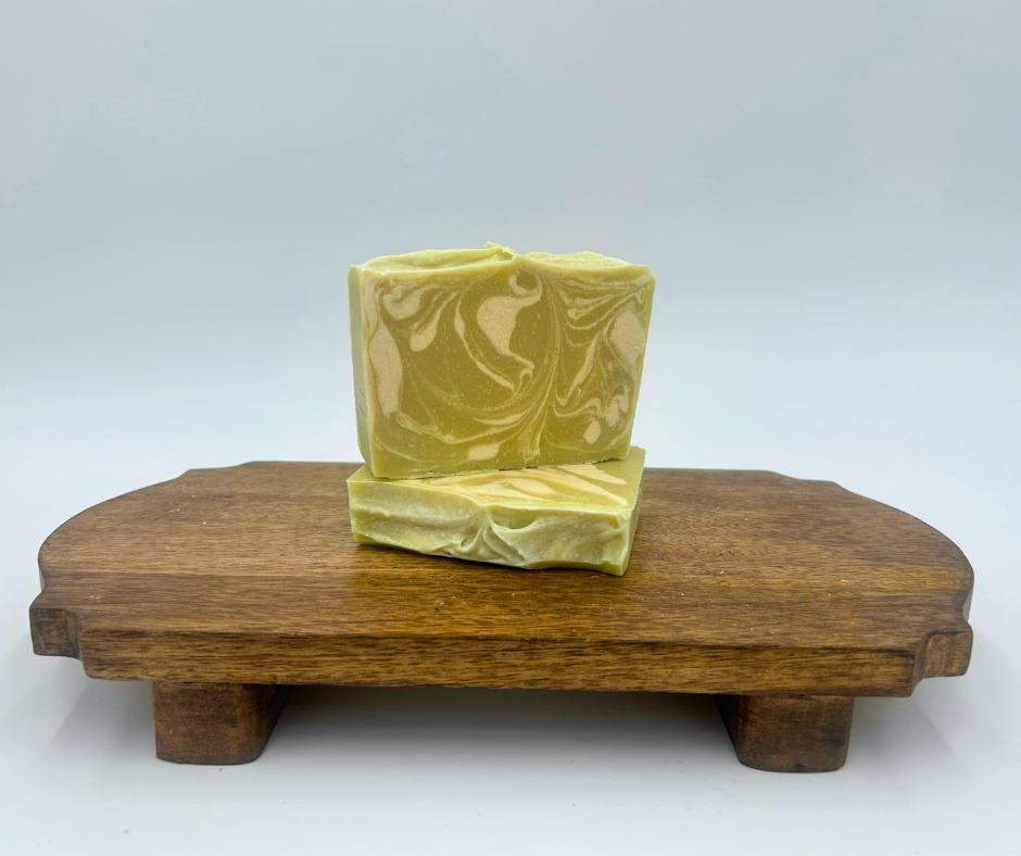 Two bars of green and white soap with marbled pattern on a wooden stand against a white background