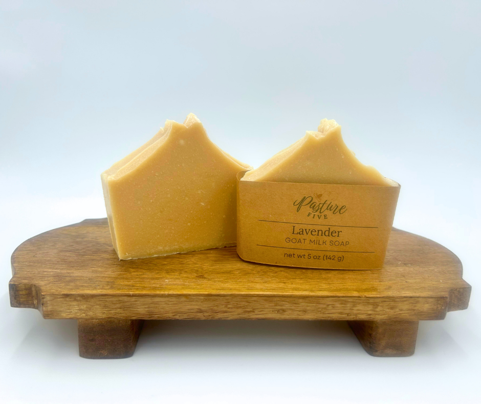 Two bars of goat milk soap on a wooden soap dish with 'Pasture Five' package.