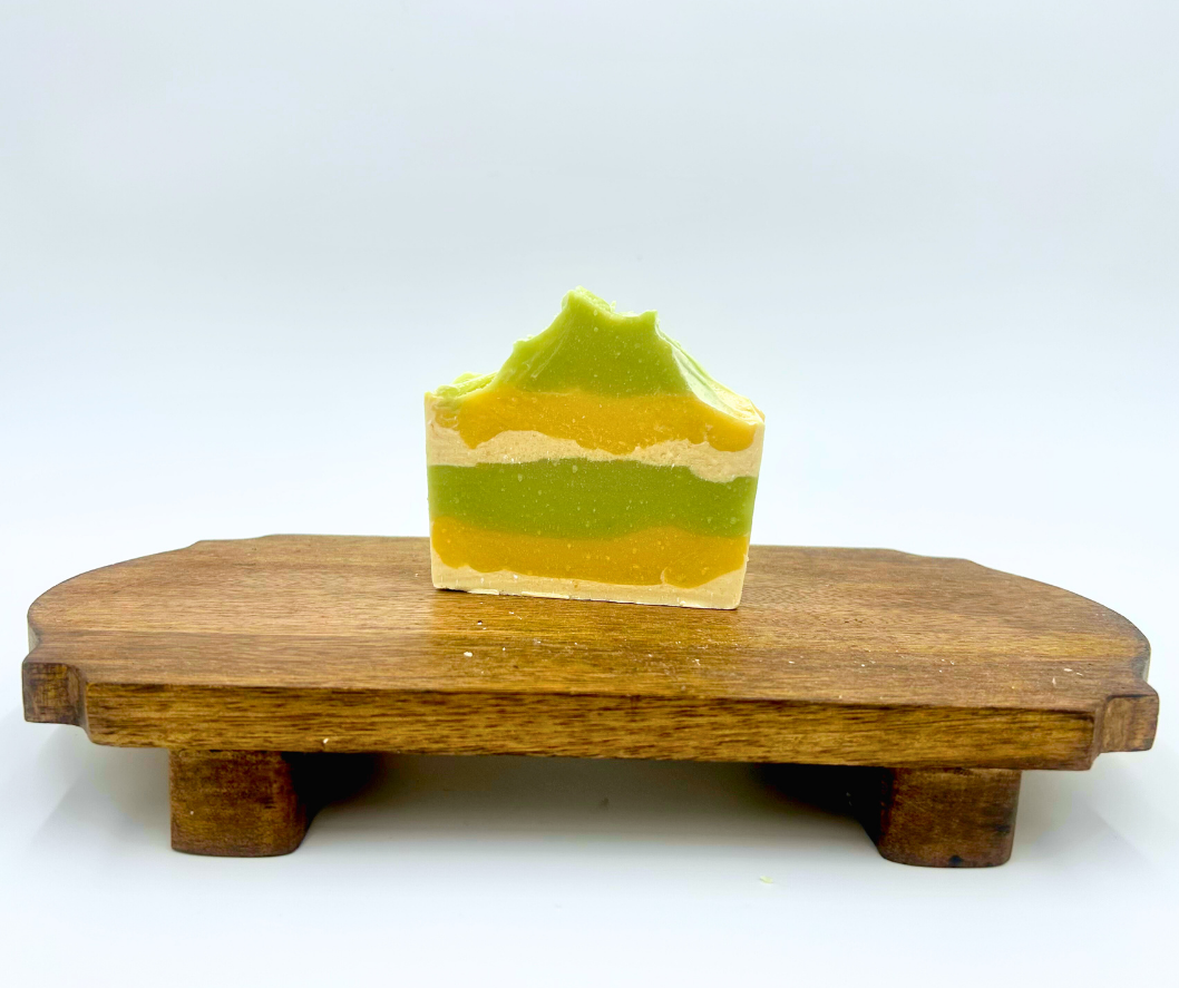 Green, white, and yellow layered goat milk soap on a wooden stand with a white background