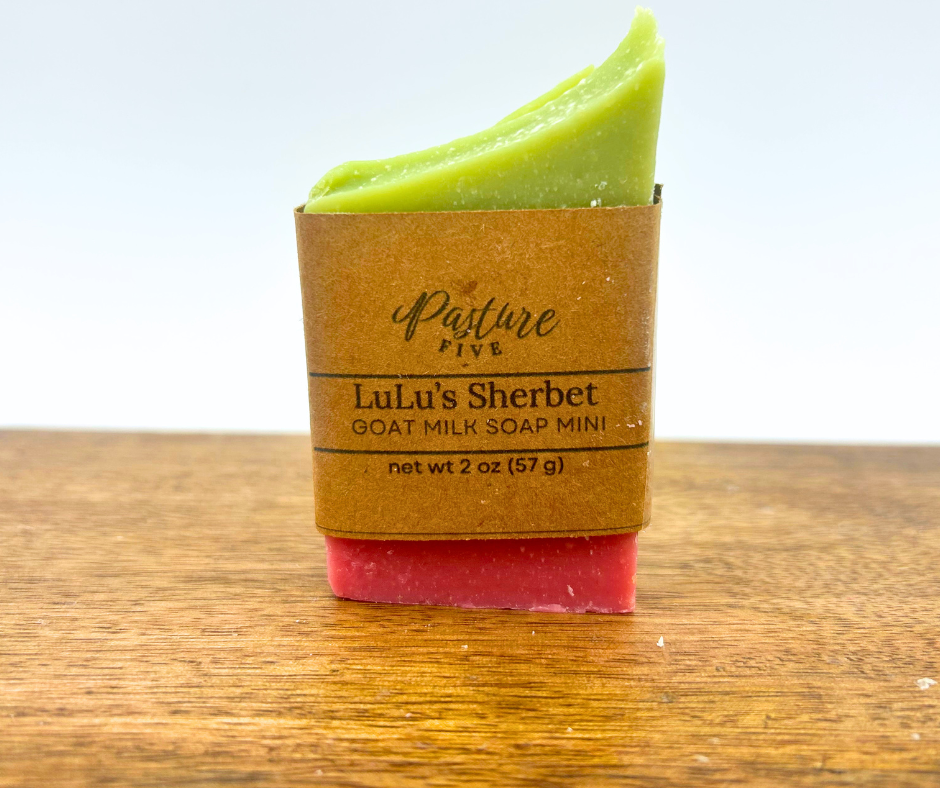 Half a bar of Green and pink goat milk soap with brown paper packaging on a wooden surface
